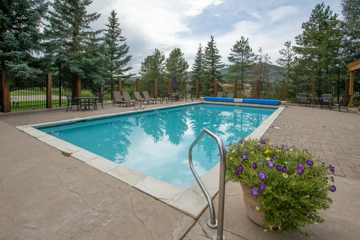 This exterior image shows a sparkling swimming pool framed by trees and lounge chairs, with a flower pot adding a pop of color. The outdoor setting is bright and inviting, embodying opportunities for recreation and social gatherings.