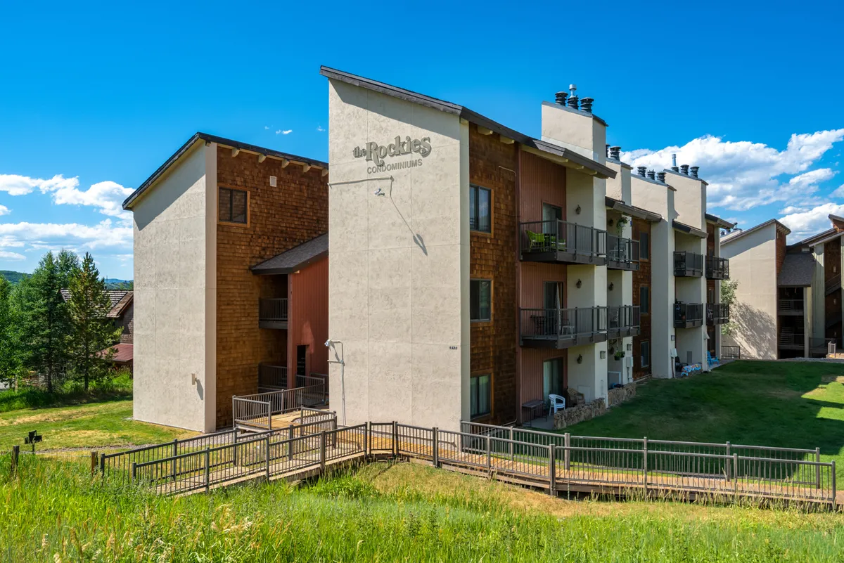 The hero image showcases the exterior of the condo building nestled in Steamboat Springs, featuring inviting balconies overlooking lush greenery, with opportunities for outdoor relaxation and socializing. The scene is bathed in warm natural light, hinting at stunning sunset views and a tranquil mountain atmosphere.