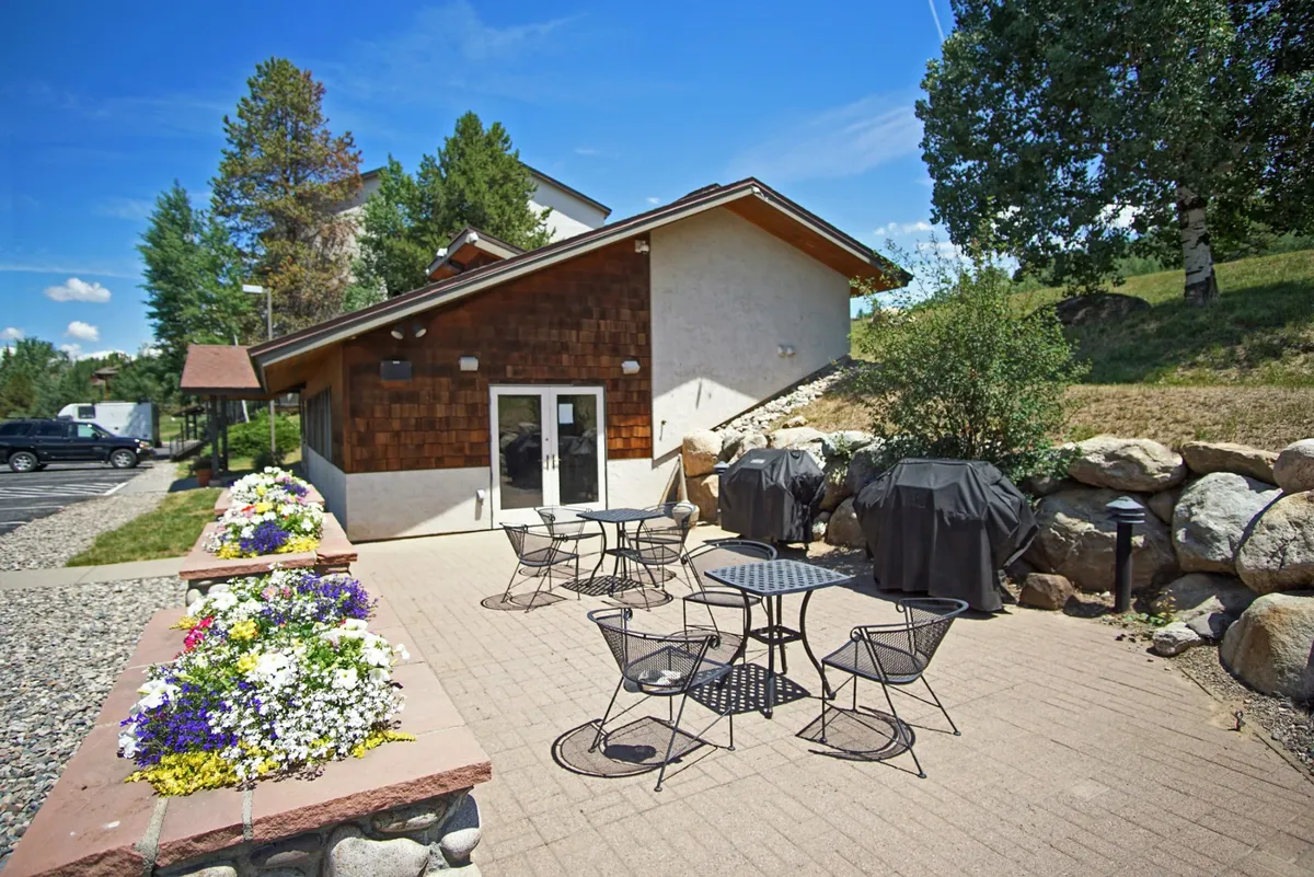A cheerful exterior patio space with a comfortable seating area, surrounded by flower beds and set against the building's facade. The space is ideal for outdoor dining, BBQs, and relaxing amidst greenery—a seamless extension of the indoor dining area.