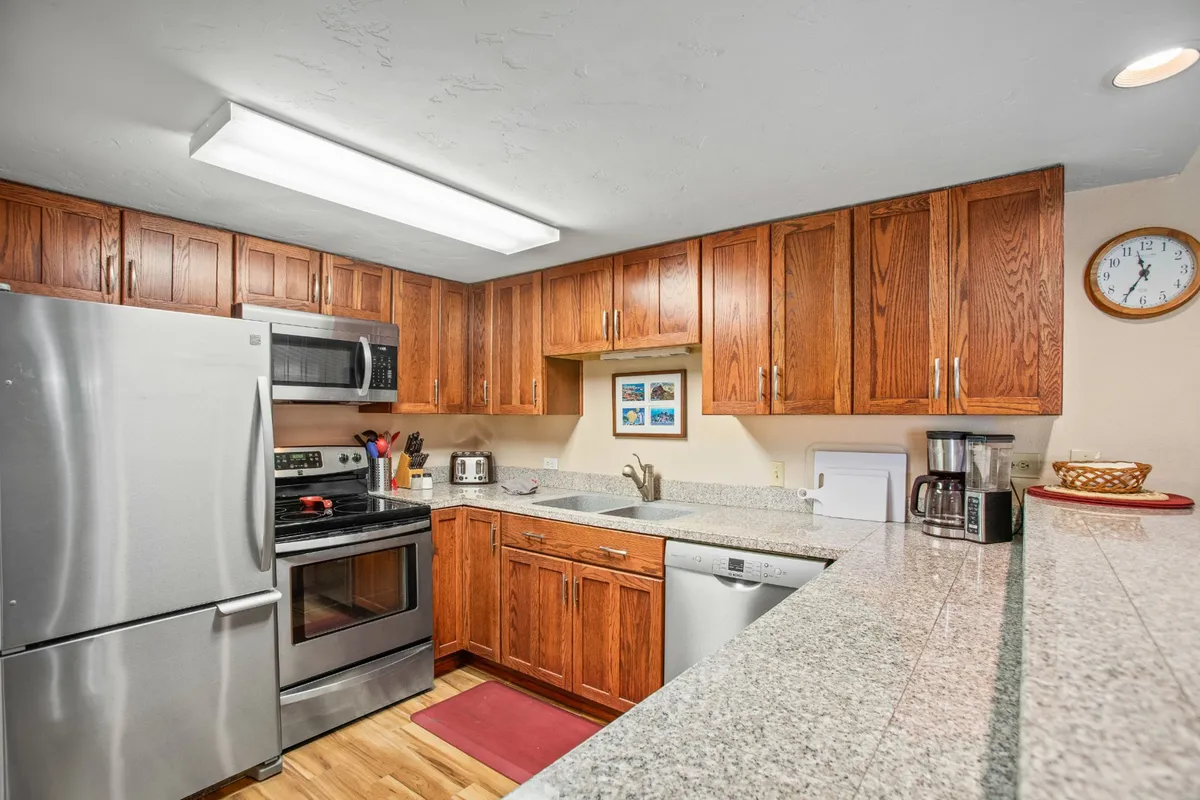 An open kitchen with matching stainless steel appliances, granite countertops, and wood cabinetry, set up for meal prep and socializing. The arrangement suggests easy movement and plenty of counter space, ideal for both everyday cooking and festive occasions.