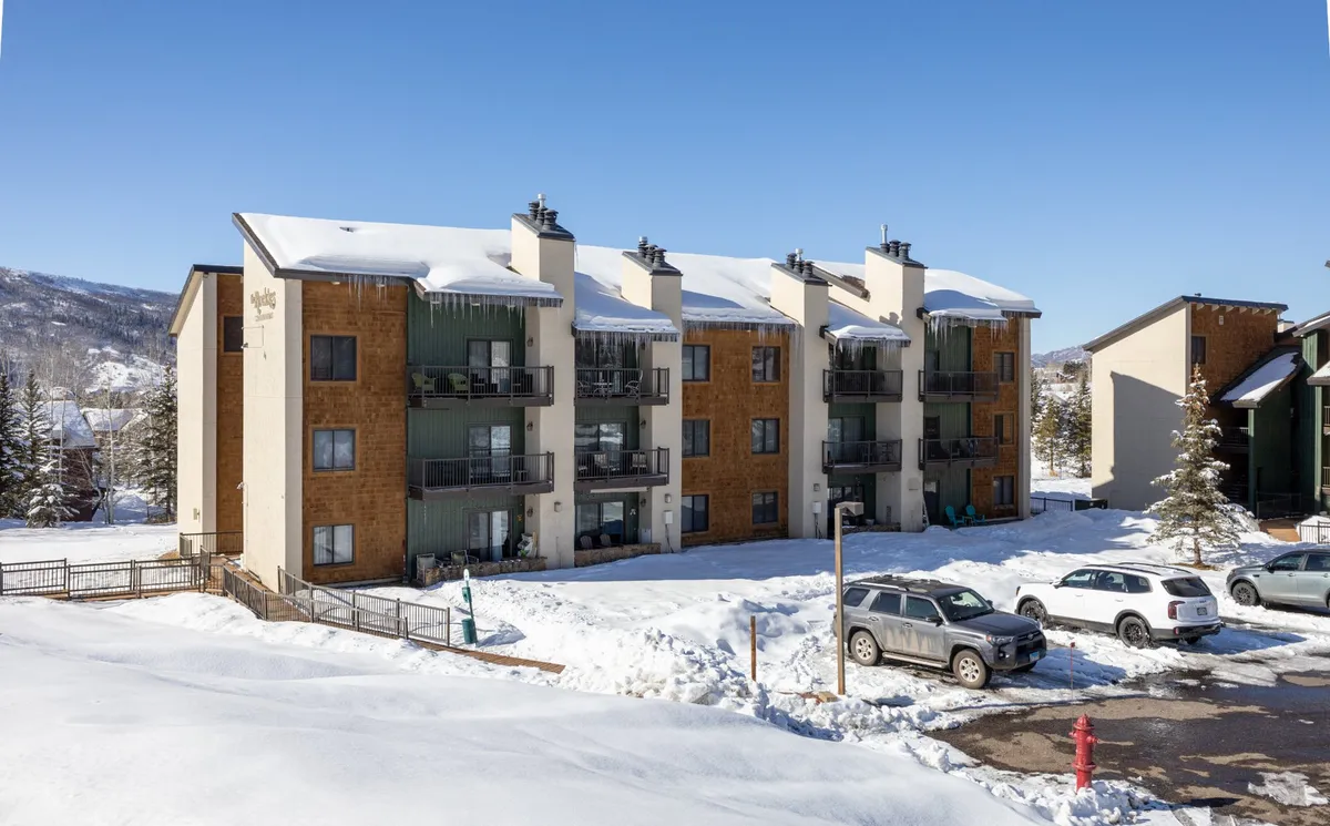 A three-story building with balconies overlooking a snow-covered ground, inviting residents to step out into the vibrant winter scene. The building’s modern design suggests comfort and cleanliness, while the snow and activity areas hint at year-round exploration and community.